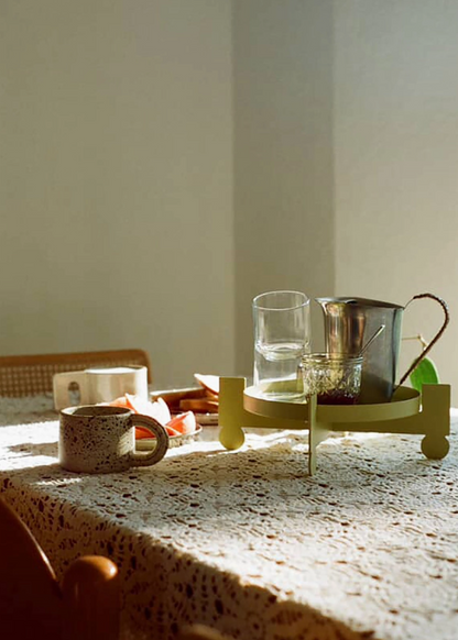 Dining table with cups, glasses, and a pitcher on a textured surface featuring a metal geometric plant stand being used as a tray for a water pitcher and cups.