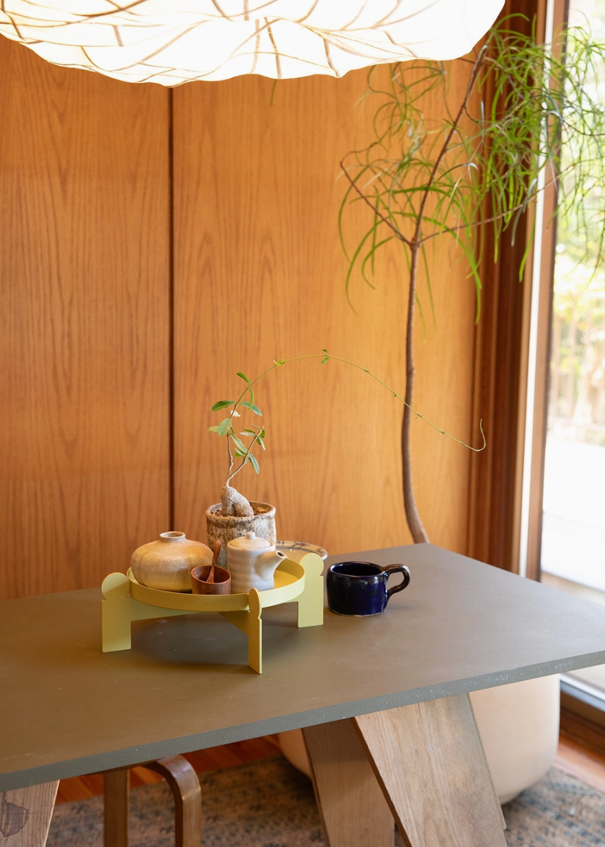 Modern interior with a wooden wall, light gray dining table with a metal geometric plant stand on it being used as a tray for decorative items.
