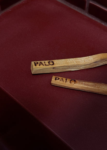 Two wooden sticks with 'Palo' engraved on them on a red surface.